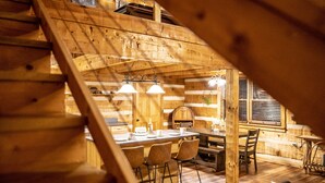Un intérieur en bois comprenant un coin repas, un escalier en bois et une fenêtre avec des stores.