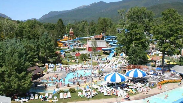 Parque acuático con toboganes y piscinas, rodeado de árboles y montañas.
