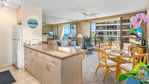 Una cocina moderna con una isla central, un comedor con sillas de mimbre y vistas a un balcón con piscina.
