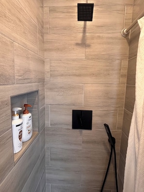 Eine Dusche mit gefliesten Wänden, einer Handbrause und zwei Flaschen Dove Duschgel auf einem Regal.