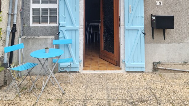Un bâtiment avec une entrée à double porte, un petit patio avec des chaises bleues et une boîte aux lettres.