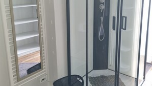 Une cabine de douche entièrement vitrée, dotée d’un banc intégré et d’un panier noir.