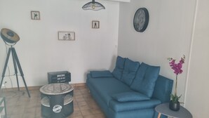 Un salon avec un canapé bleu, une petite table ronde, un lampadaire sur pied et une plante en pot.