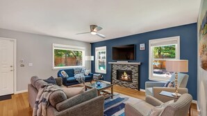 Una sala de estar con chimenea, paredes azules y un ventilador de techo.