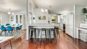 Een moderne keuken met een centraal eiland, barkrukken en een eethoek met blauwe stoelen.