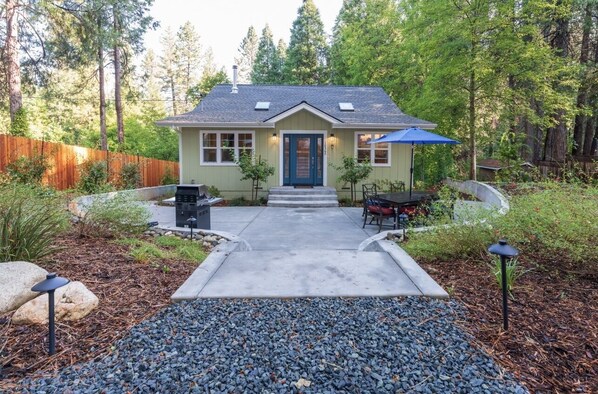 A single-story house with a front porch, a patio with outdoor furniture, and a wooden fence surrounding the property. - New, Cozy home- walk to downtown! (Nevada City)