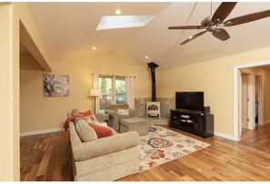 A living room with a sofa, armchairs, a fireplace, a television, and a ceiling fan. - New, Cozy home- walk to downtown! (Nevada City)
