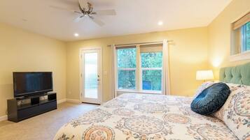 A bedroom with a bed, a television, a ceiling fan, and a window with curtains.
