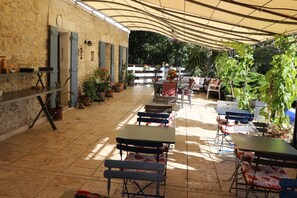 An outdoor patio with tables and chairs, surrounded by potted plants and a stone wall. - Mas Des Cerisiers (Avignon)