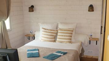 A bedroom with a bed, wooden floor, a TV, and a small table with a bottle.