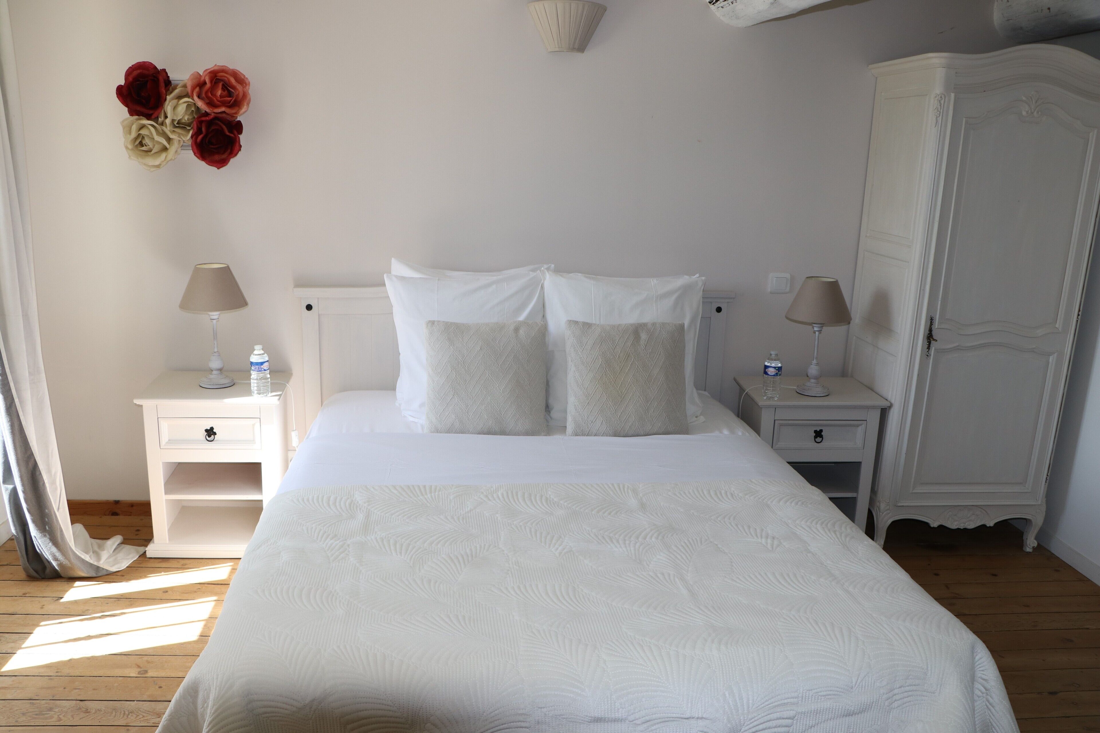 A neatly arranged bedroom with a large bed, two bedside tables with lamps, a wardrobe, and a wall decoration of flowers.