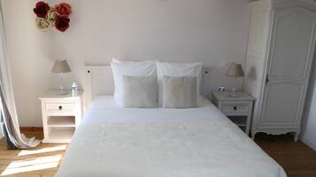 A neatly arranged bedroom with a large bed, two bedside tables with lamps, a wardrobe, and a wall decoration of flowers.