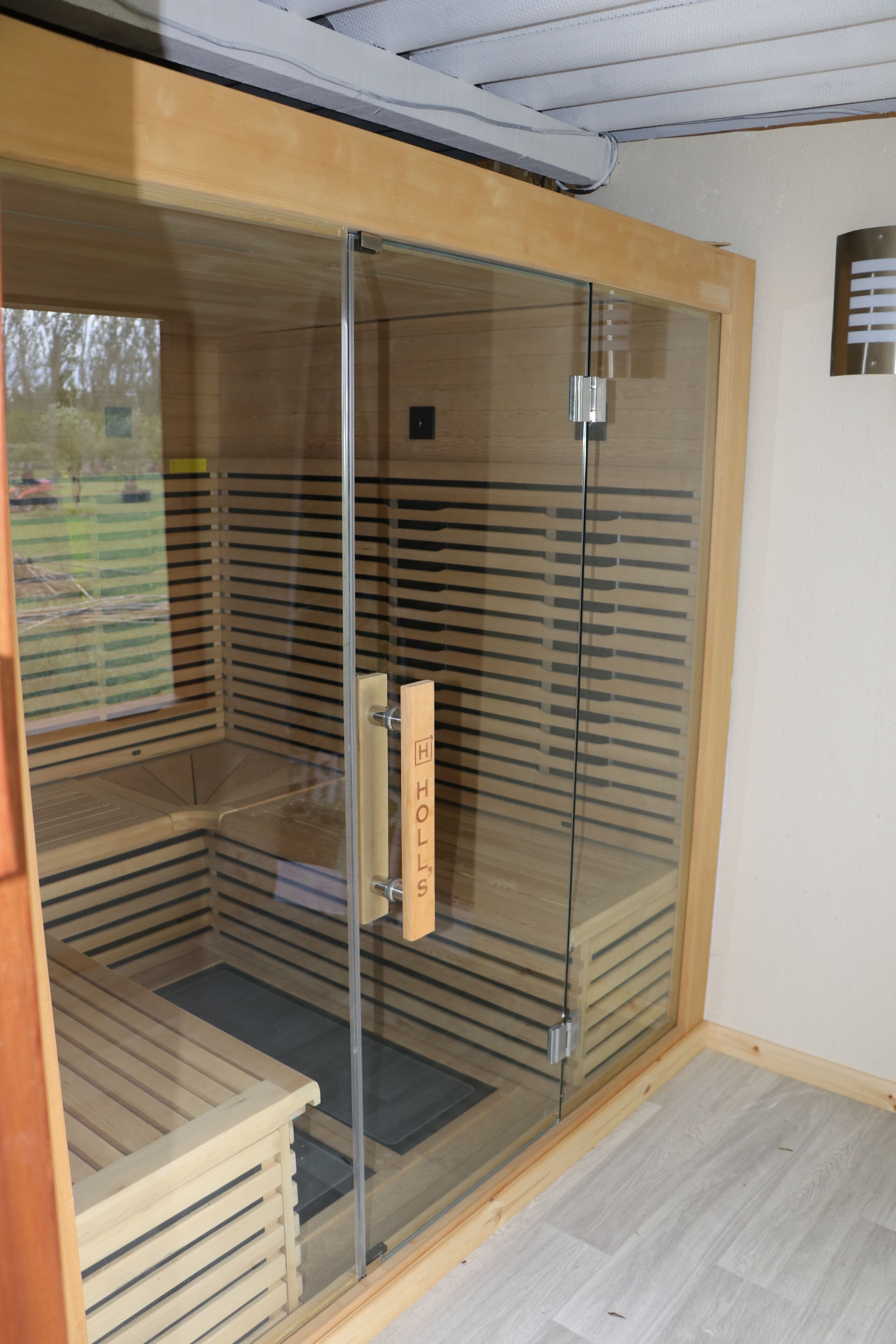 Eine Sauna mit Glasfront, einer Holzbank und einer Tür mit Griff.