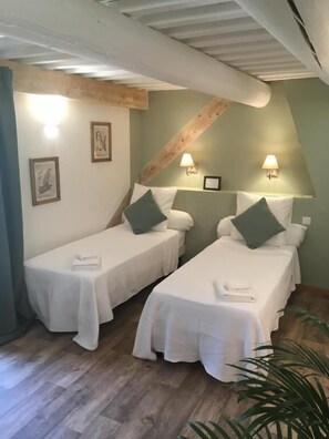 A room with two single beds, each with a pillow and a folded towel. There are wall-mounted lamps and framed pictures on the walls. - Mas Des Cerisiers (Avignon)