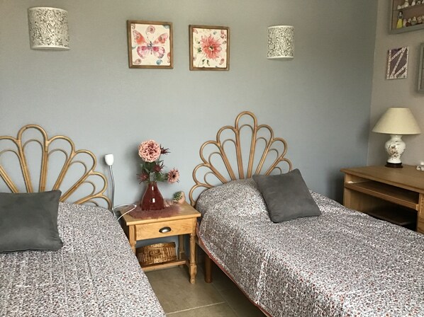 A bedroom with two beds, a nightstand, a lamp, and two wall-mounted lamps.