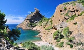 A coastal landscape with rocky cliffs, clear turquoise waters, and a sandy beach.