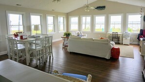 Amplia sala de estar con un ventanal grande, comedor con mobiliario blanco y cocina con encimera y armarios blancos.