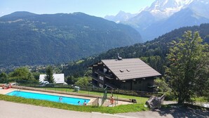 Un refugio de montaña con piscina, rodeado de exuberante vegetación y montañas.