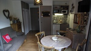 Un espacio habitable compacto con sofá, mesa de comedor, sillas, kitchenette y televisor.