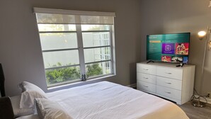 A bedroom with a large bed, a TV on a dresser, and a window with blinds. - WaterFront,walk to Beach,Pool 1BR 1B & Parking (Fort Lauderdale)