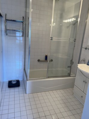 A bathroom with a glass-enclosed shower, a white sink, and a weighing scale on the floor.