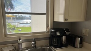 A kitchen with a stainless steel sink, a coffee maker, a toaster, and a window overlooking a pool and greenery. - WaterFront,walk to Beach,Pool 1BR 1B & Parking (Fort Lauderdale)