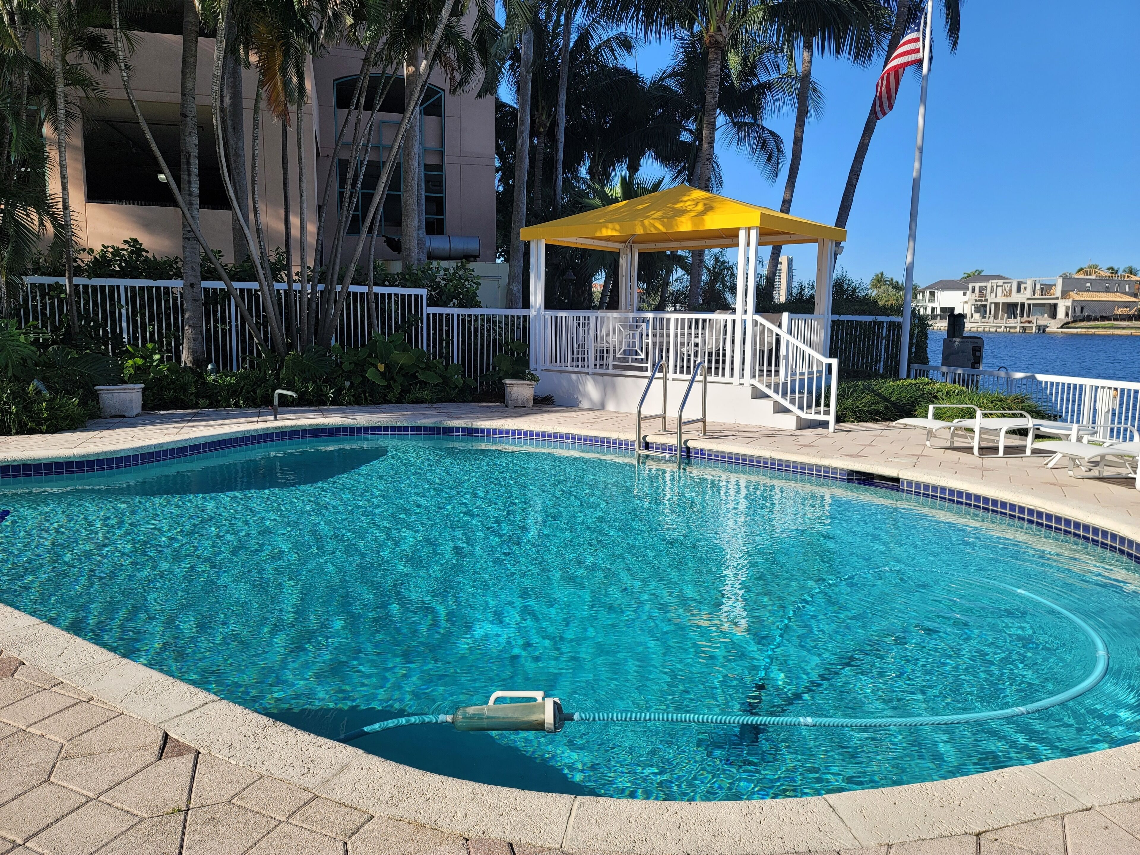 A clear swimming pool with a yellow gazebo, white railing, and a view of the sea.