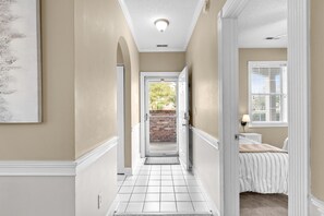 A hallway with a door leading to a room with a bed and a window.