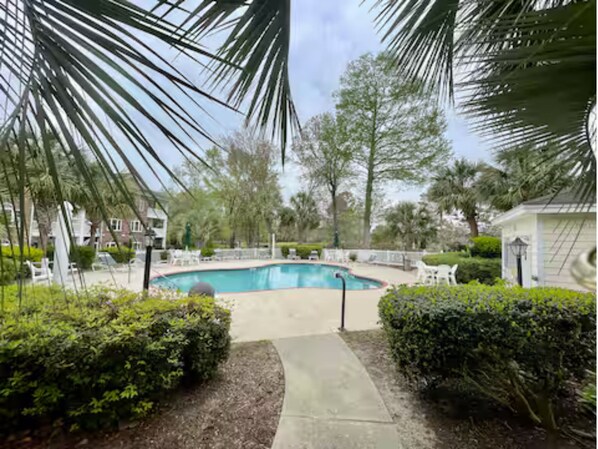 A swimming pool surrounded by greenery and a paved walkway.