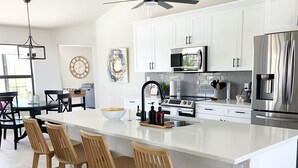 A modern kitchen with a large island, white cabinetry, stainless steel appliances, and wooden bar stools. - Cape Villa Family Friendly Canal front 4 Bedroom Southern Facing Heated Pool Spa (Cape Coral)