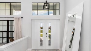A white interior with a double door, a window with a curtain, and a hanging light fixture. - Cape Villa Family Friendly Canal front 4 Bedroom Southern Facing Heated Pool Spa (Cape Coral)