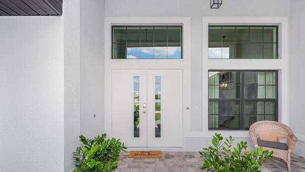 A clean, white exterior with a double door, two windows, and a wicker chair. - Cape Villa Family Friendly Canal front 4 Bedroom Southern Facing Heated Pool Spa (Cape Coral)