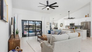 A modern living room with a sofa, a coffee table, and a TV on a wooden stand. There is a dining area with a table and chairs, and a kitchen with a refrigerator and microwave. - Cape Villa Family Friendly Canal front 4 Bedroom Southern Facing Heated Pool Spa (Cape Coral)