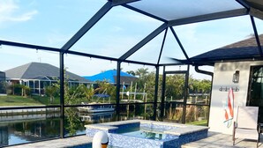 A swimming pool with a swan float, clear blue water, and a covered area with a view of houses and greenery. - Cape Villa Family Friendly Canal front 4 Bedroom Southern Facing Heated Pool Spa (Cape Coral)