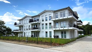 Un edificio residencial de varios pisos con balcones, un camino de entrada pavimentado y un patio cercado.