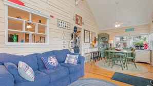 Ein gemütliches Wohnzimmer mit einem blauen Sofa, einem gemusterten Teppich und einem Essbereich mit grünem Tisch und Stühlen.