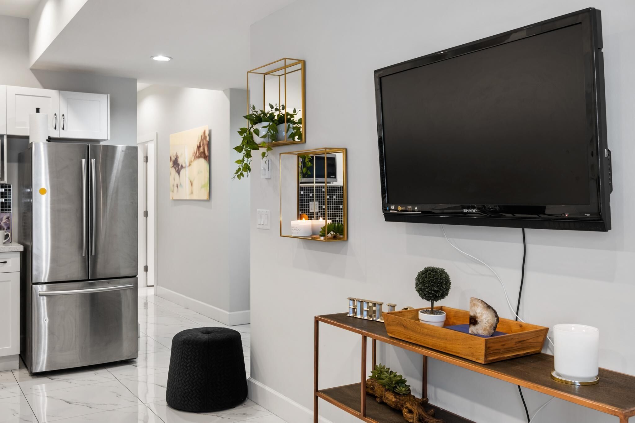 Een moderne keuken met roestvrijstalen apparatuur, een zwarte tv aan de muur en een houten console met decoratieve objecten.