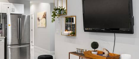 Een moderne keuken met roestvrijstalen apparatuur, een zwarte tv aan de muur en een houten console met decoratieve objecten.