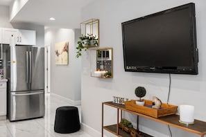 A modern kitchen with stainless steel appliances, a black TV mounted on the wall, and a wooden console table with decorative items.