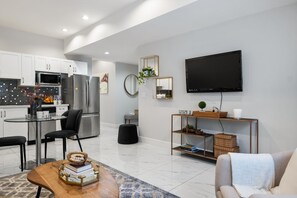 A modern kitchen with white cabinets, a stainless steel refrigerator, and a dining area with a glass table and black chairs. - Quaint 2 Bedrooms and Sofa Bed Suite  (Langley Township)