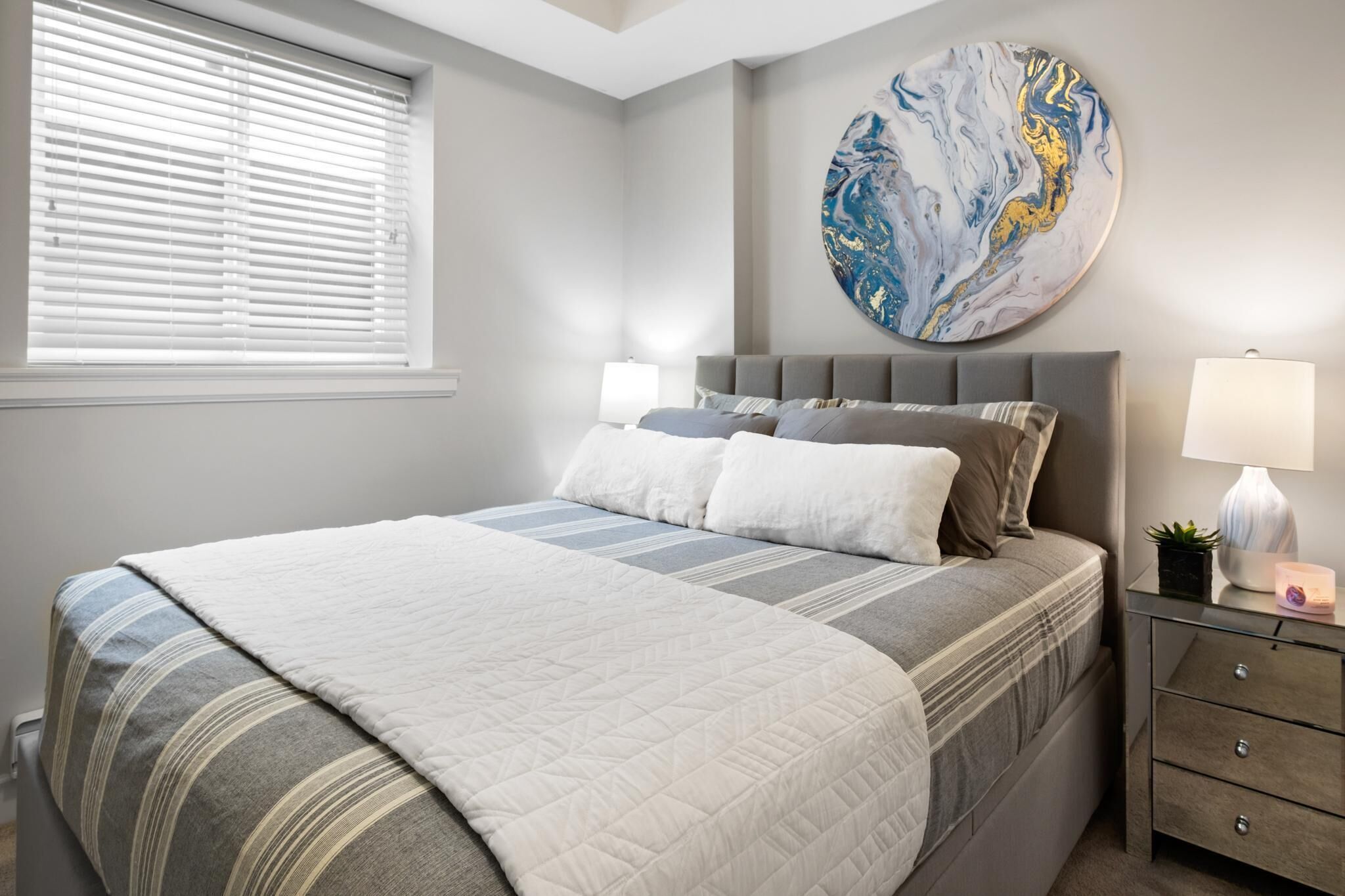 A bedroom with a bed, bedside tables, a wall art piece, and a window with blinds.