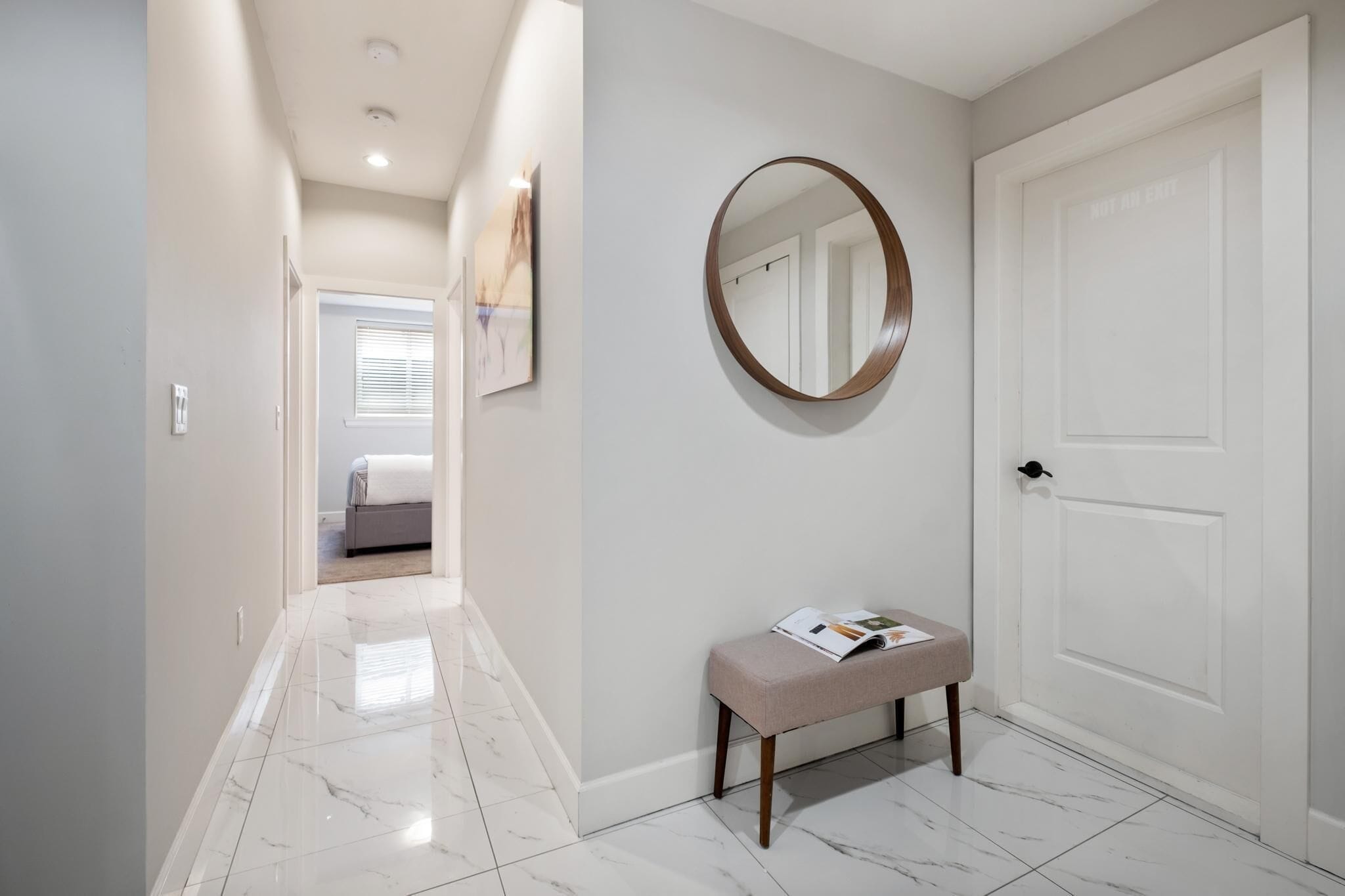 A hallway with a bench, a round mirror, and a white door.
