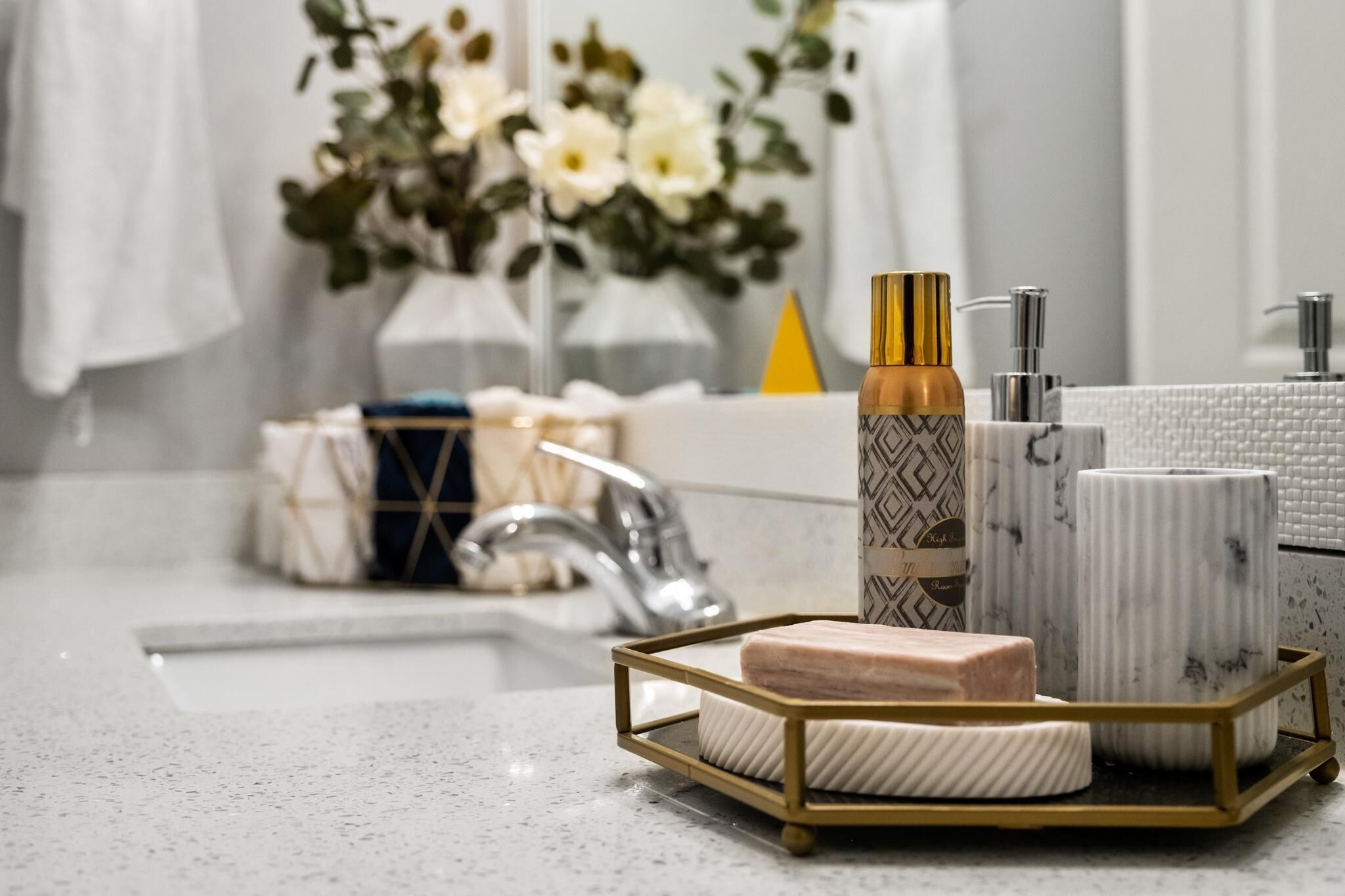 A bathroom with a white marble sink, a gold-framed soap dish, and a vase with flowers.
