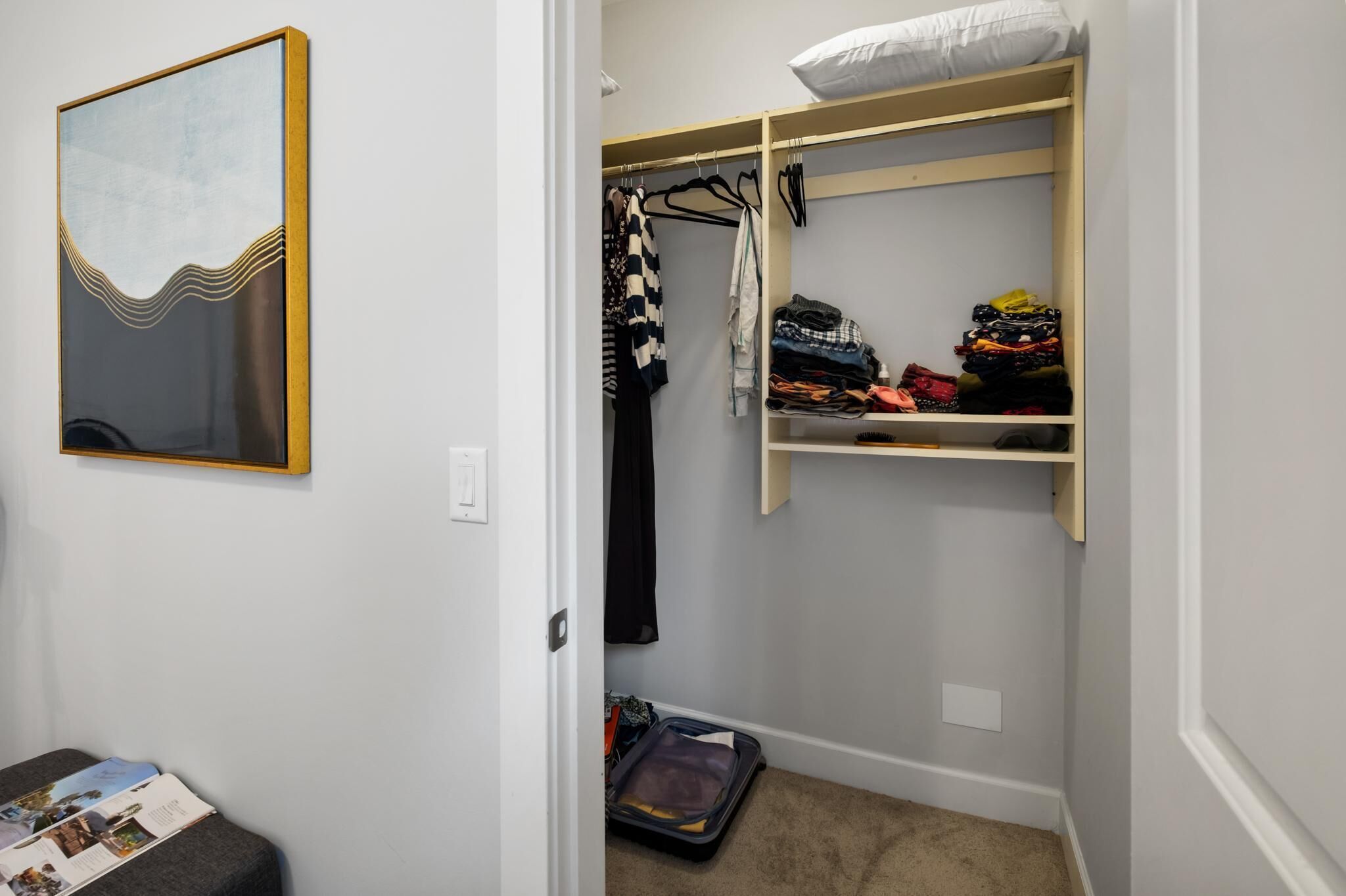A walk-in closet with hanging space and shelves, a bed with a pillow, and a suitcase on the floor.