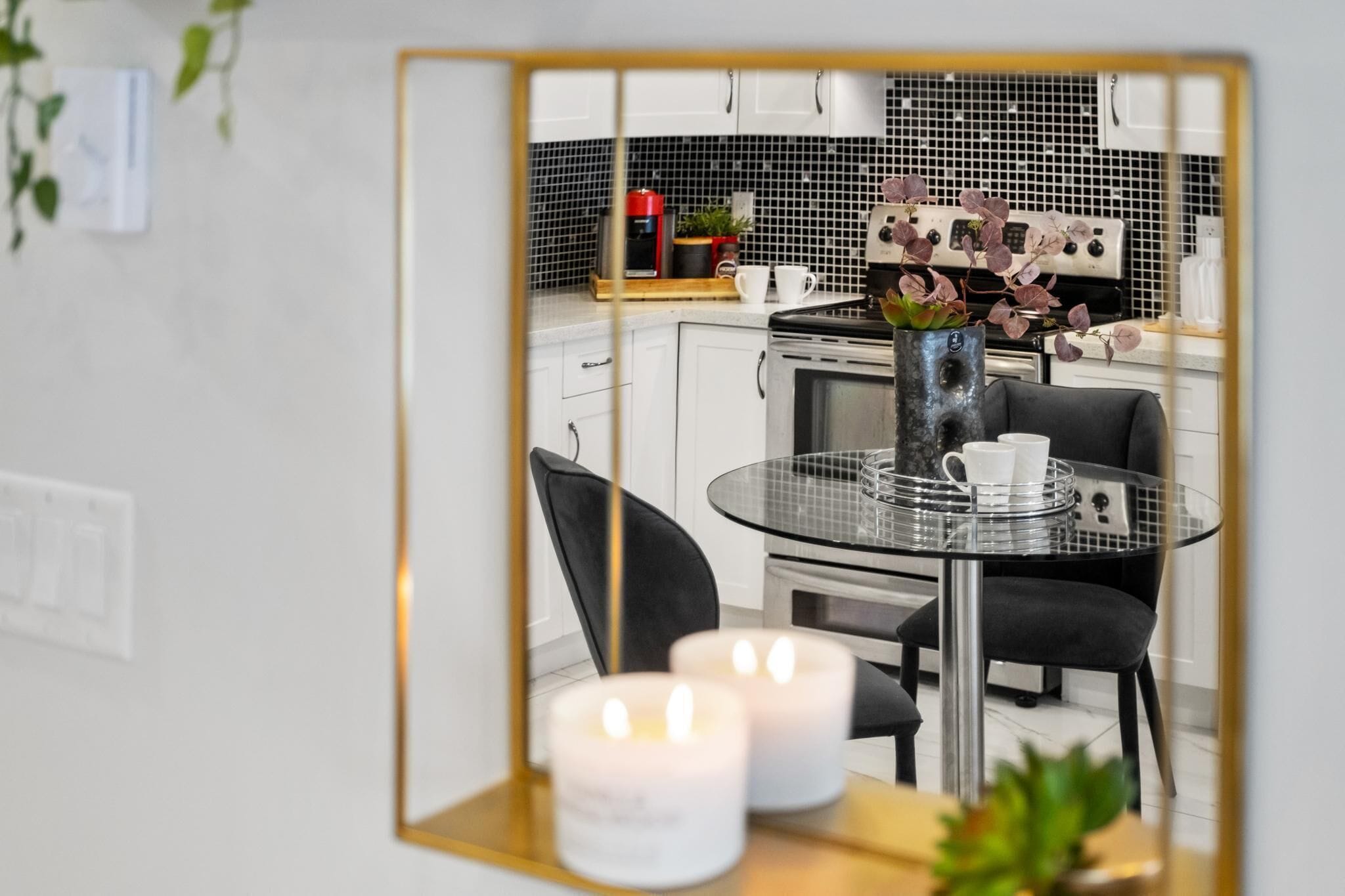 A modern kitchen with white cabinets, a black and white backsplash, and a round glass table with two chairs.