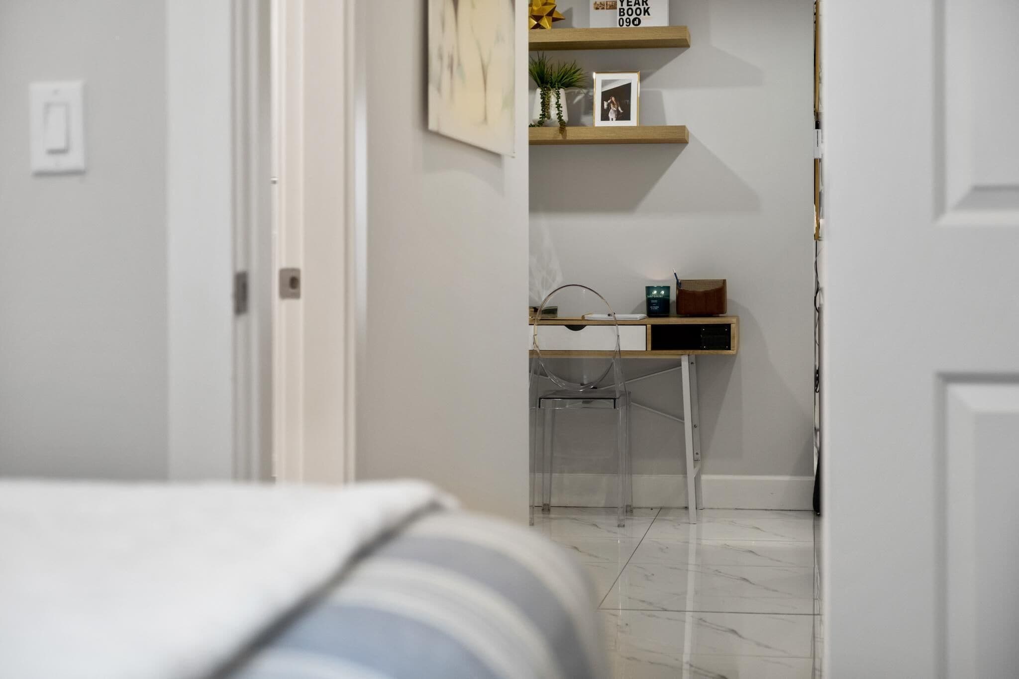 Un pasillo que conduce a una habitación con escritorio, silla y estanterías con objetos.