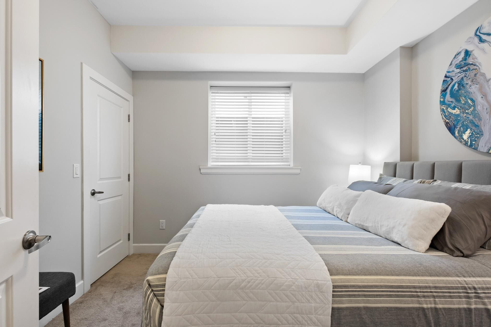 Un dormitorio con una cama, una ventana con persianas, una puerta y una pared decorada con una obra de arte circular.