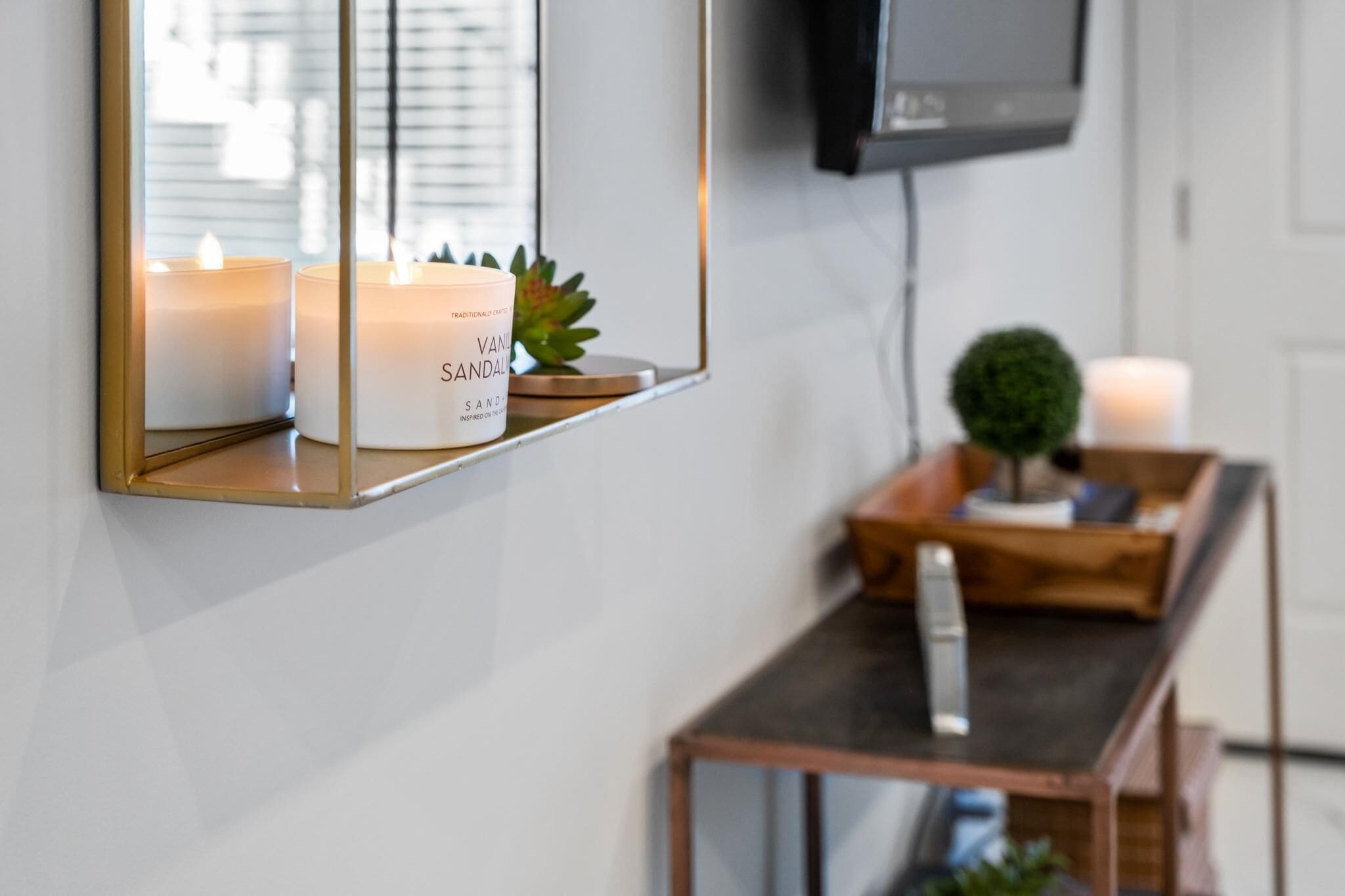 Un espejo refleja velas, una planta pequeña y un televisor en una pared.
