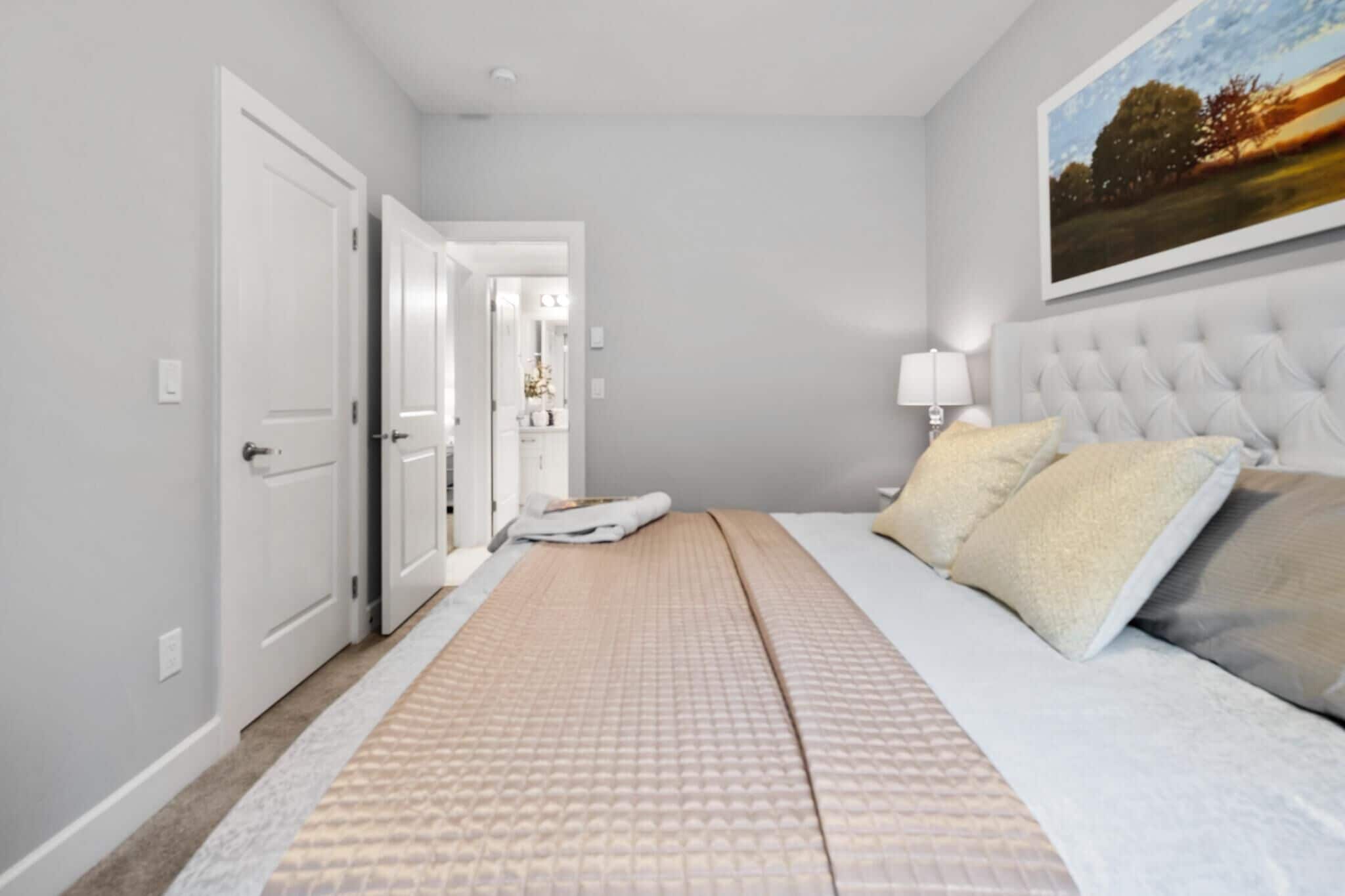 A bedroom with a bed, a nightstand, a lamp, and a door leading to another room.