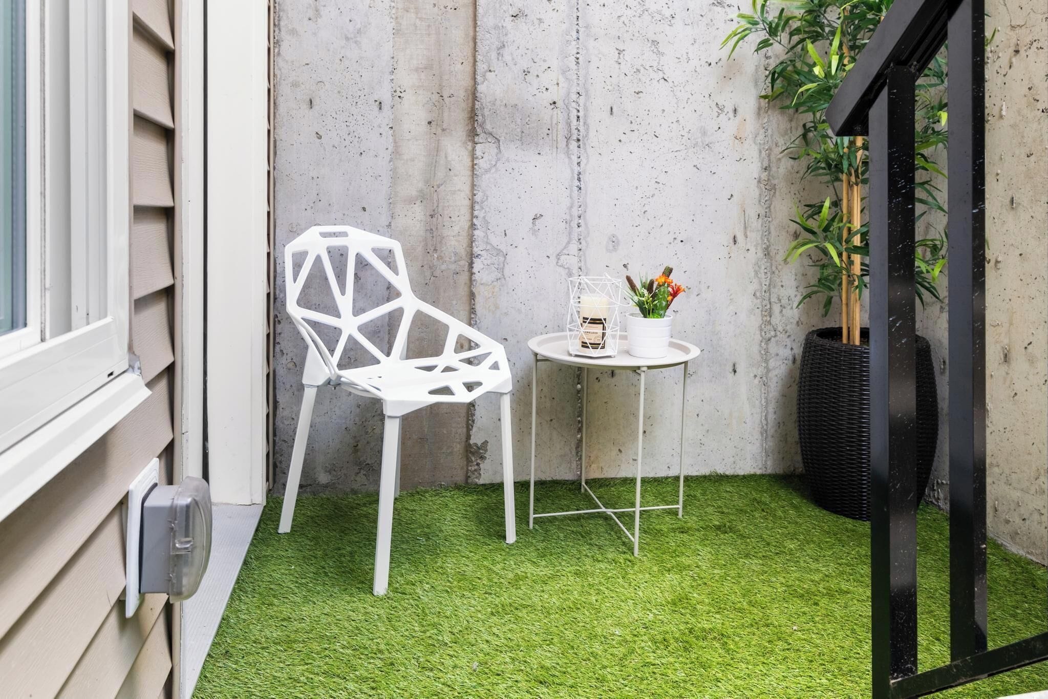 Un pequeño espacio al aire libre con una silla blanca y una mesa, rodeado de césped artificial y un muro de concreto.
